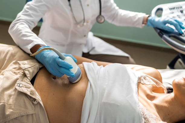 Medical professional wearing gloves uses an ultrasound probe on a patient’s bare midsection during an abdominal ultrasound examination.